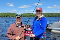 Chloe and Mark ristow in a boat on Percy Lake holding the Bass Tournament fishing trophy.