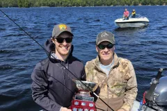 Mark and Connor Ristow stand in their boat holding up a fishing trophy.