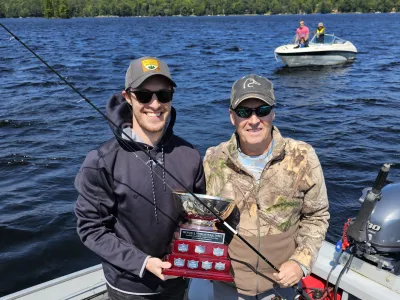 Mark and Connor Ristow stand in their boat holding up a fishing trophy.