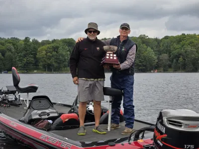 Lou and Joe stand in a boat holding the Percy Lake bass tournament trophy.