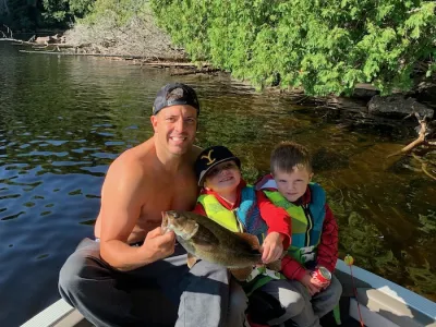 A man and two young boys wearing lifejackets hold up a bass in a boat.
