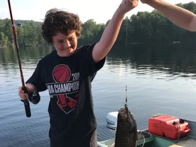 Charlie Houston standing on a dock and holding a fishing rod with a fish on the hook