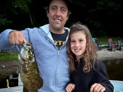 A man holds a fish next to a young girl while standing on a dock.