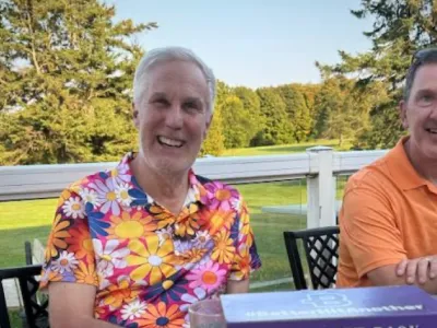 Rob wears a colorful shirt with flowers on it. A brewery gift pack sits on the table in front of him.