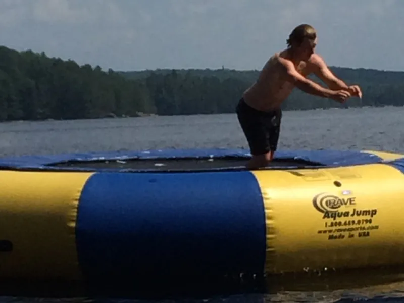 Someone bouncing on the blue and yellow Rave water trampoline on the lake