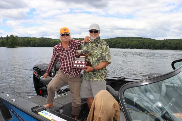 Two men in a boat, holding a fishing trophy.