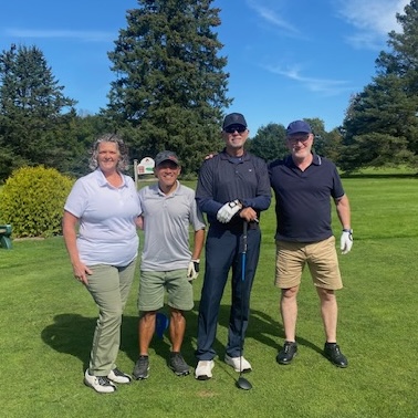 Four golfers, a woman and three men, pose on a golf green.